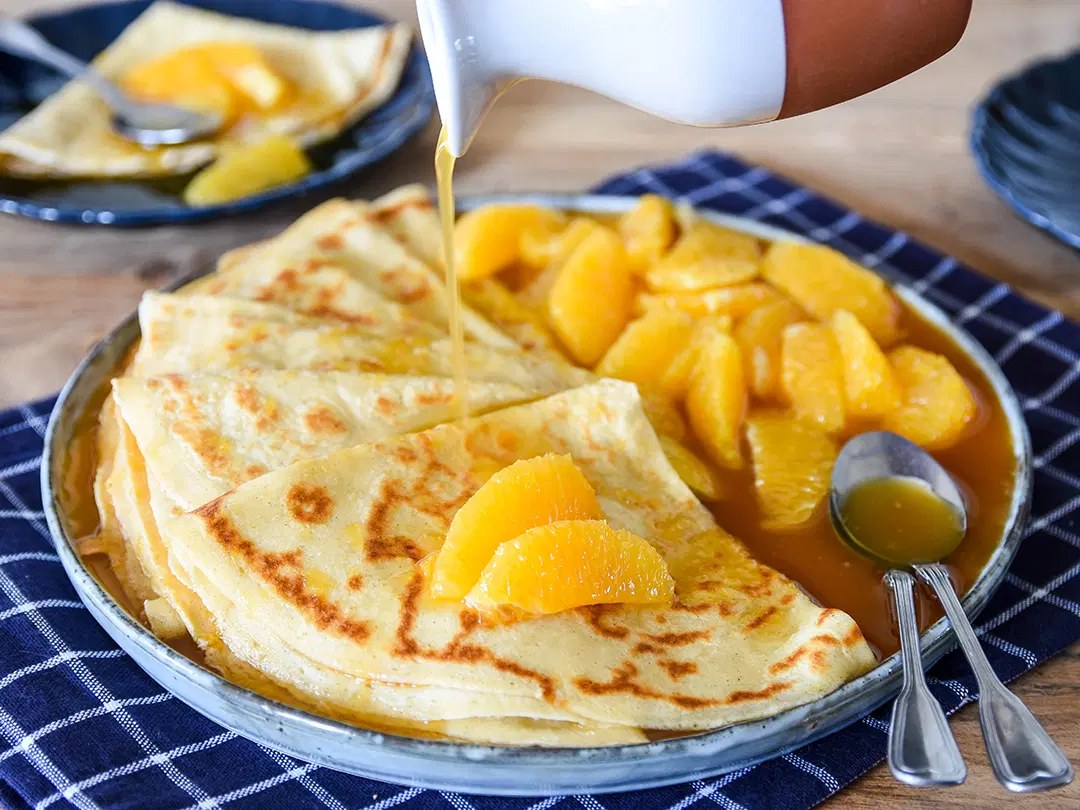 Crêpe Suzette pliée en quatre nappée de sauce à l'orange et flambée dans une poêle